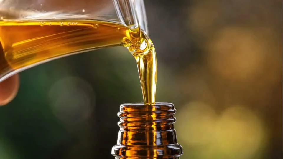 Golden Ayurvedic oil pouring into an amber glass bottle in slow motion macro